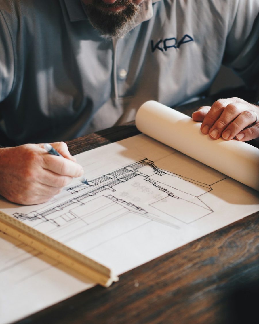 Builder drafting a house plan with a pencil and scale ruler